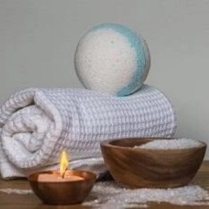 Bath bomb on rolled towel, candle and bowl of bath salts